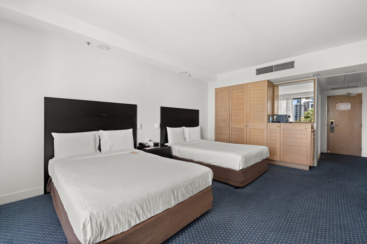 Camera d'albergo con due letti, un armadio e un bagno visibile attraverso una porta aperta.