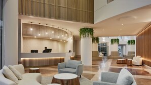 A spacious lobby with a reception desk, seating areas, and a high ceiling with wooden slats.