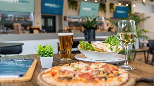 Una mesa de comedor con pizza, una copa de cerveza, un bol de ensalada y una copa de vino.