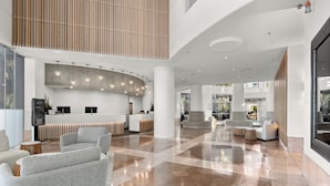 A spacious lobby with a reception desk, seating area, and a high ceiling with hanging lights.