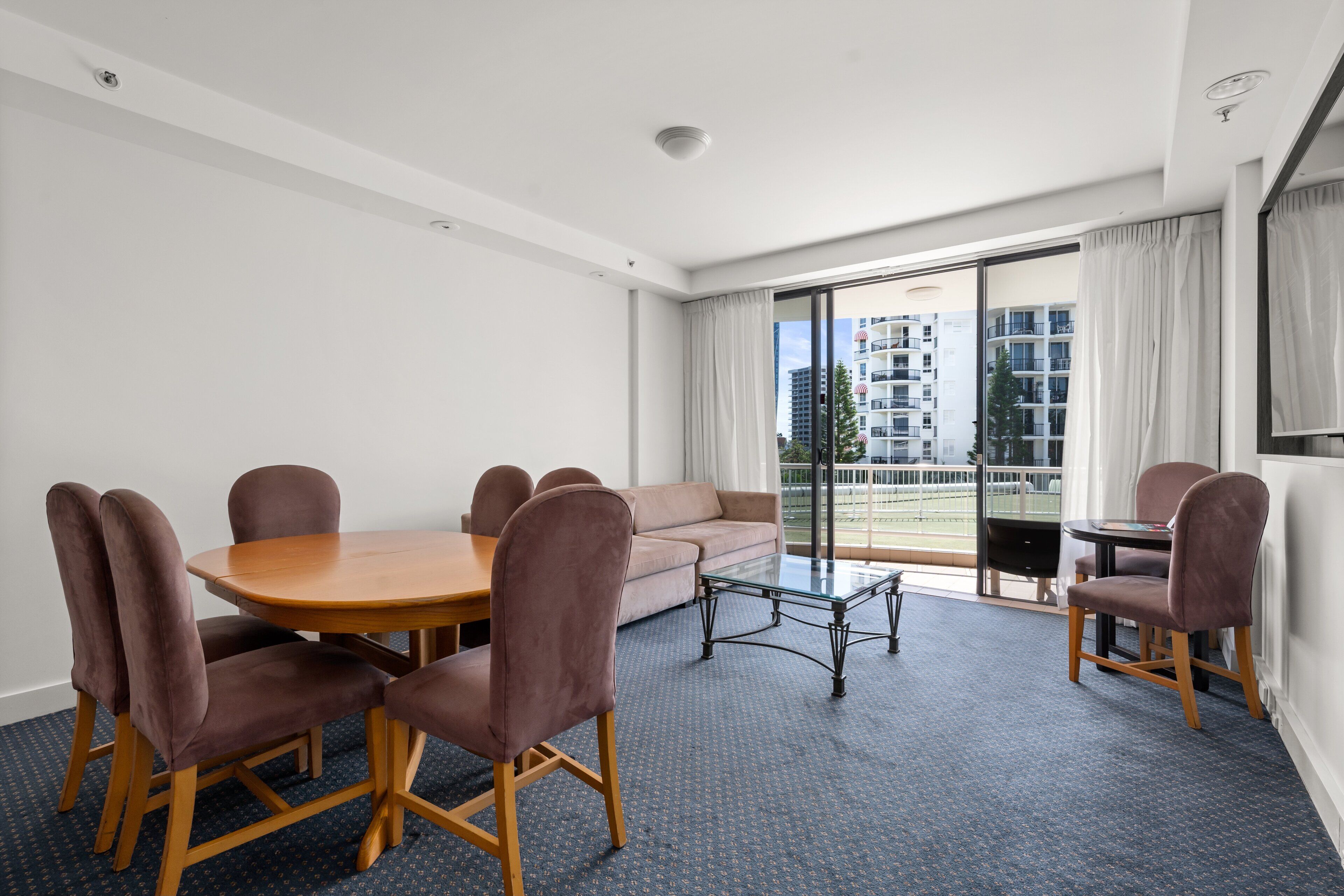 A modern hotel room with a dining area, a sofa, and a balcony with a view of the city.