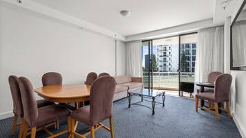 A modern hotel room with a dining area, a sofa, and a balcony with a view of the city.