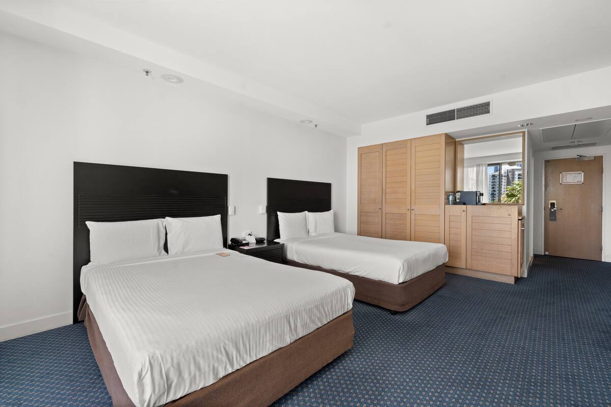 A hotel room with two beds, a wardrobe, and a bathroom visible through an open door.