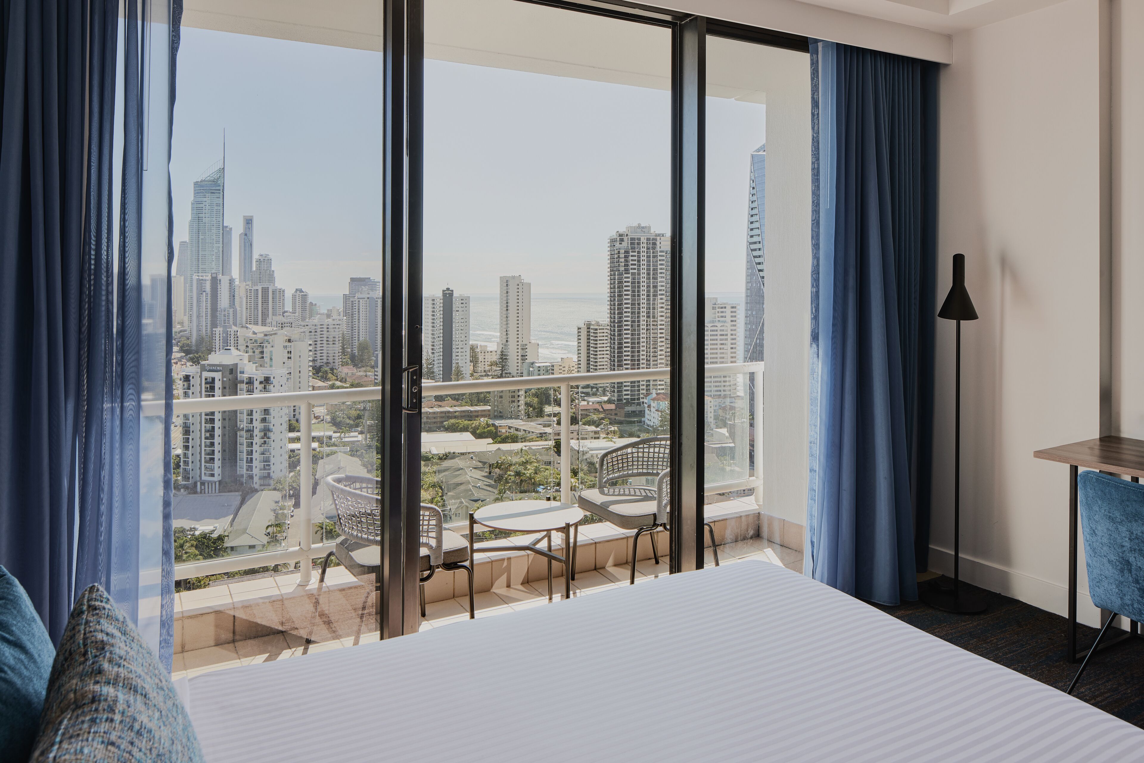 A hotel room with a large balcony, a bed, a desk, and a chair.