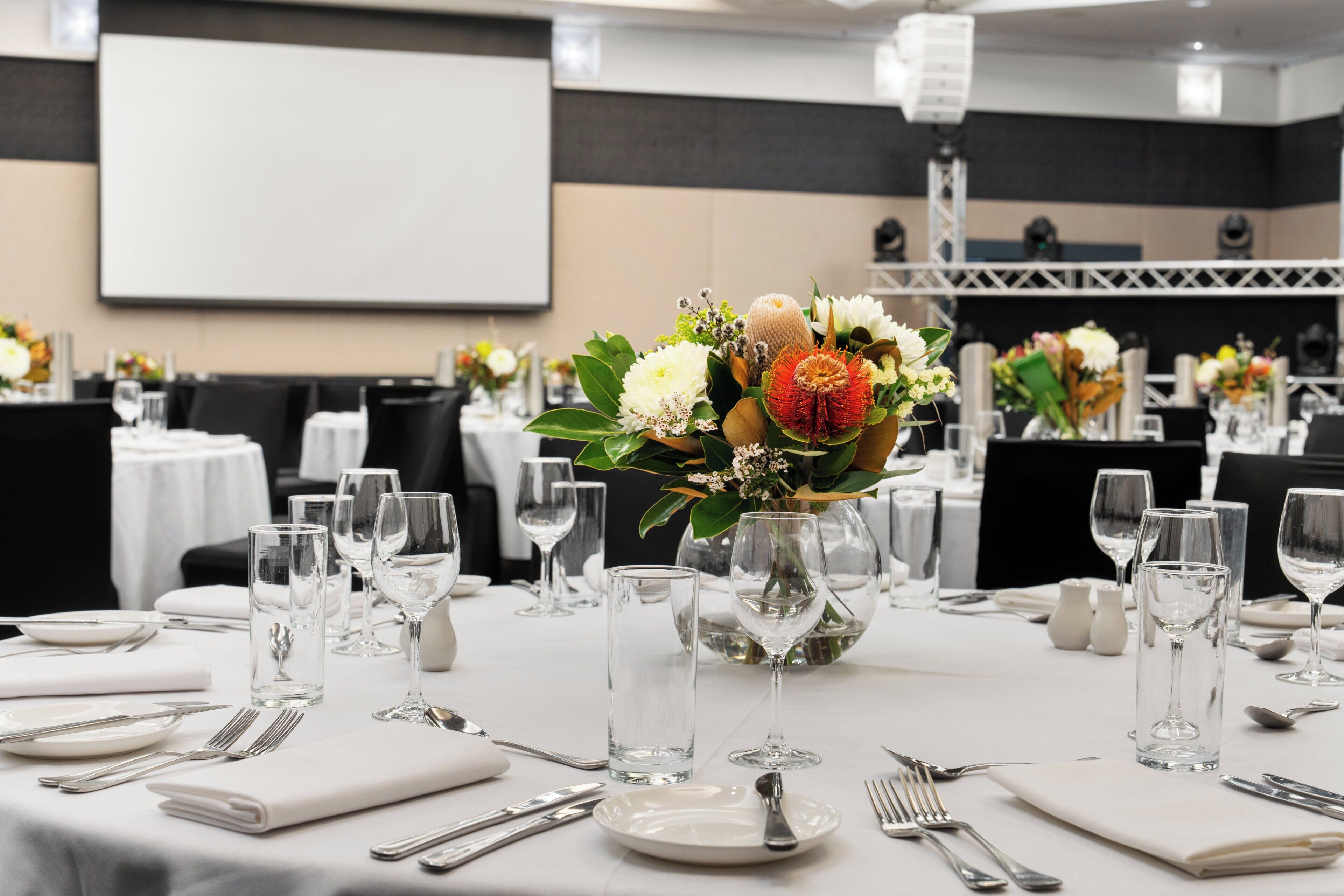 Un salón de banquetes con mesas dispuestas para comer, con copas de cristal transparente y manteles blancos.