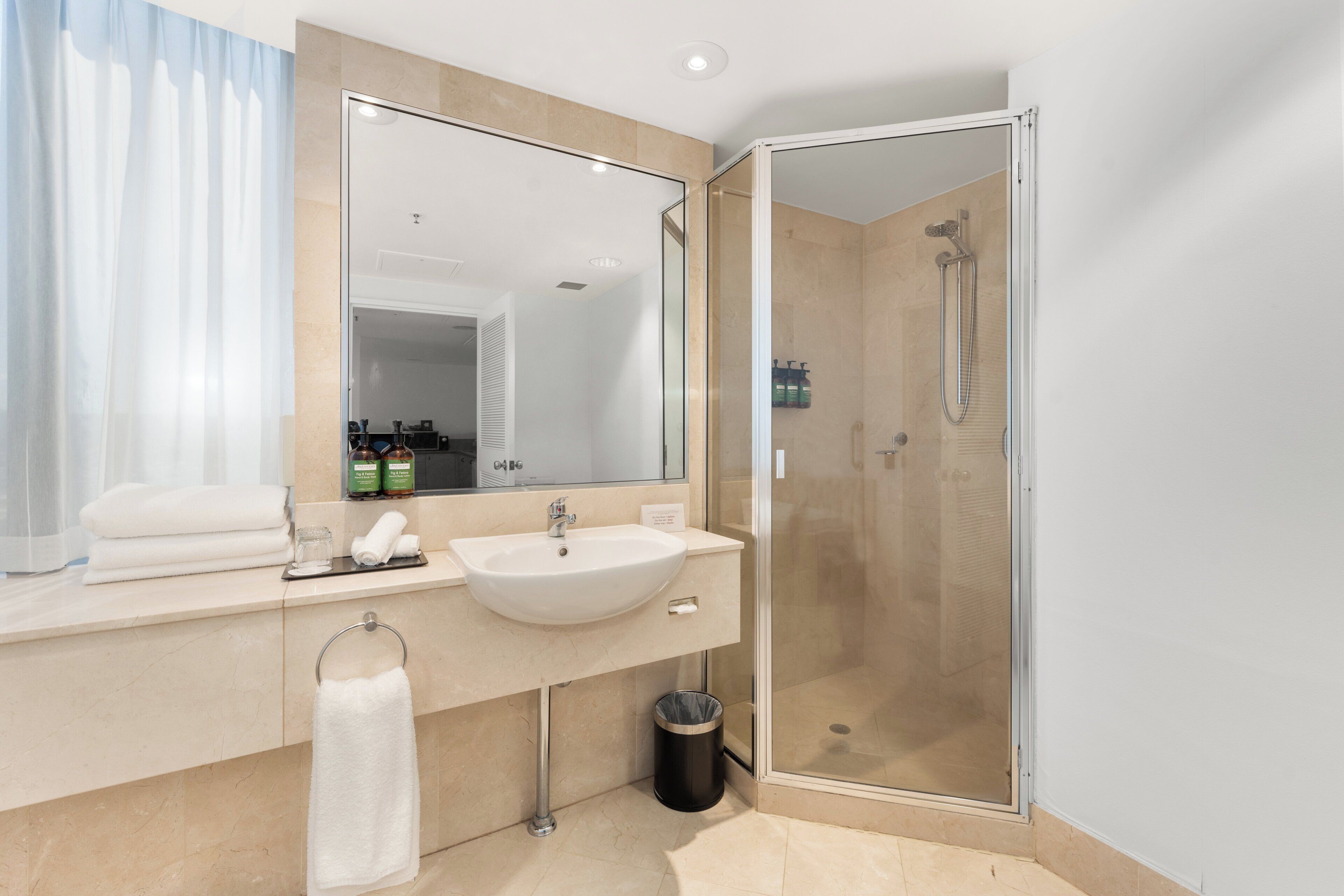 Un baño moderno con un espejo grande, un lavamanos y una ducha con mampara de cristal.