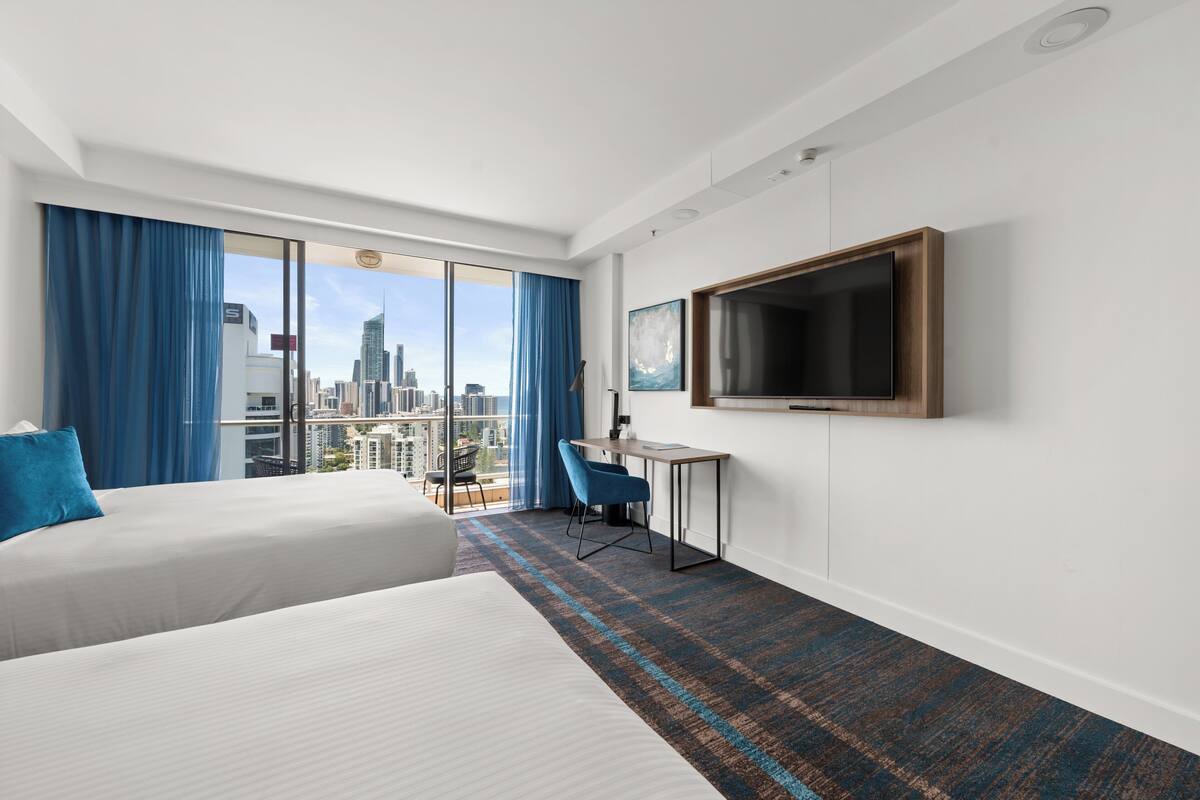 A hotel room with a large bed, a desk, a TV, and a view of the cityscape.