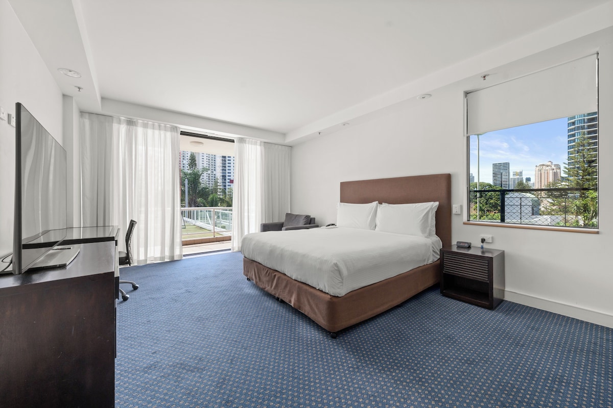 Camera d'albergo con un letto grande, una scrivania con un computer, una sedia, un tavolino e una finestra con vista sulla città.