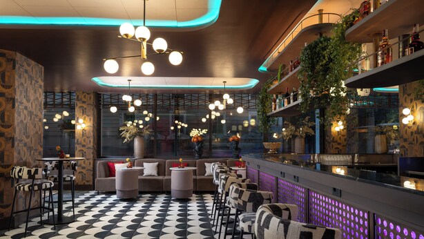 A modern bar area with a checkered floor, round hanging lights, and a bar counter with shelves of bottles.