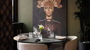 A dining table set with glasses, a vase with a flower, and a painting on the wall.
