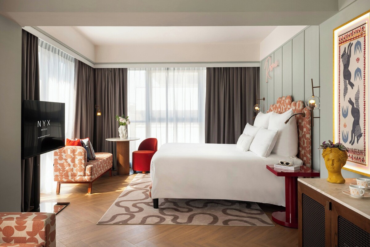 Ein Hotelzimmer mit Bett, Fernseher, einem roten Sessel, einem kleinen Tisch und einer Wanddekoration.