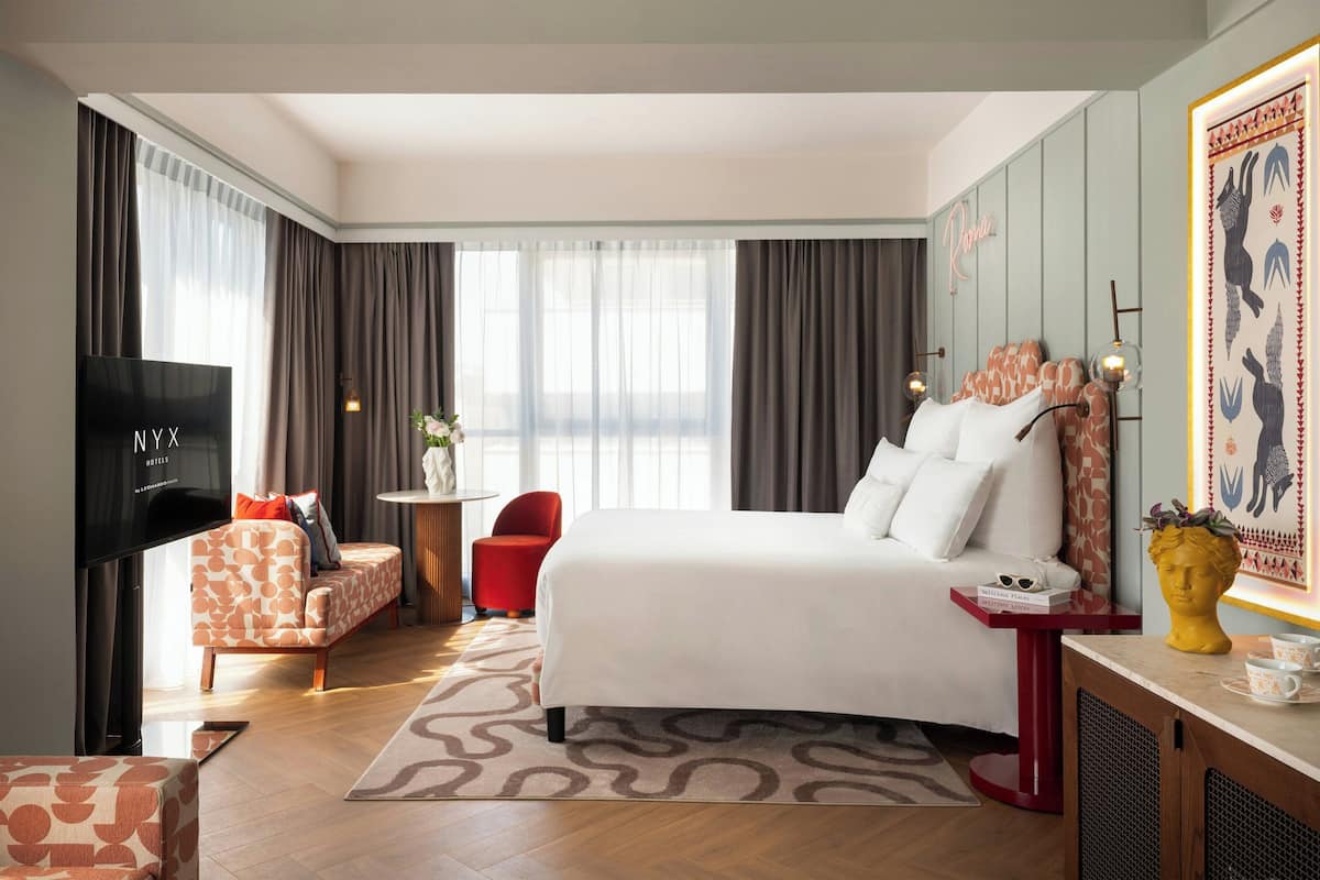 Ein Hotelzimmer mit Bett, Fernseher, einem roten Sessel, einem kleinen Tisch und einer Wanddekoration.
