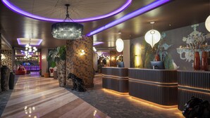 A modern lobby with a reception desk, a large chandelier, and a bar area in the background.