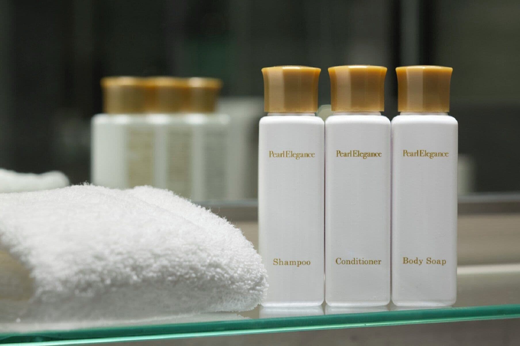 Tres botellas de productos Pearl Elegance: champú, acondicionador y jabón corporal, sobre una encimera de baño.
