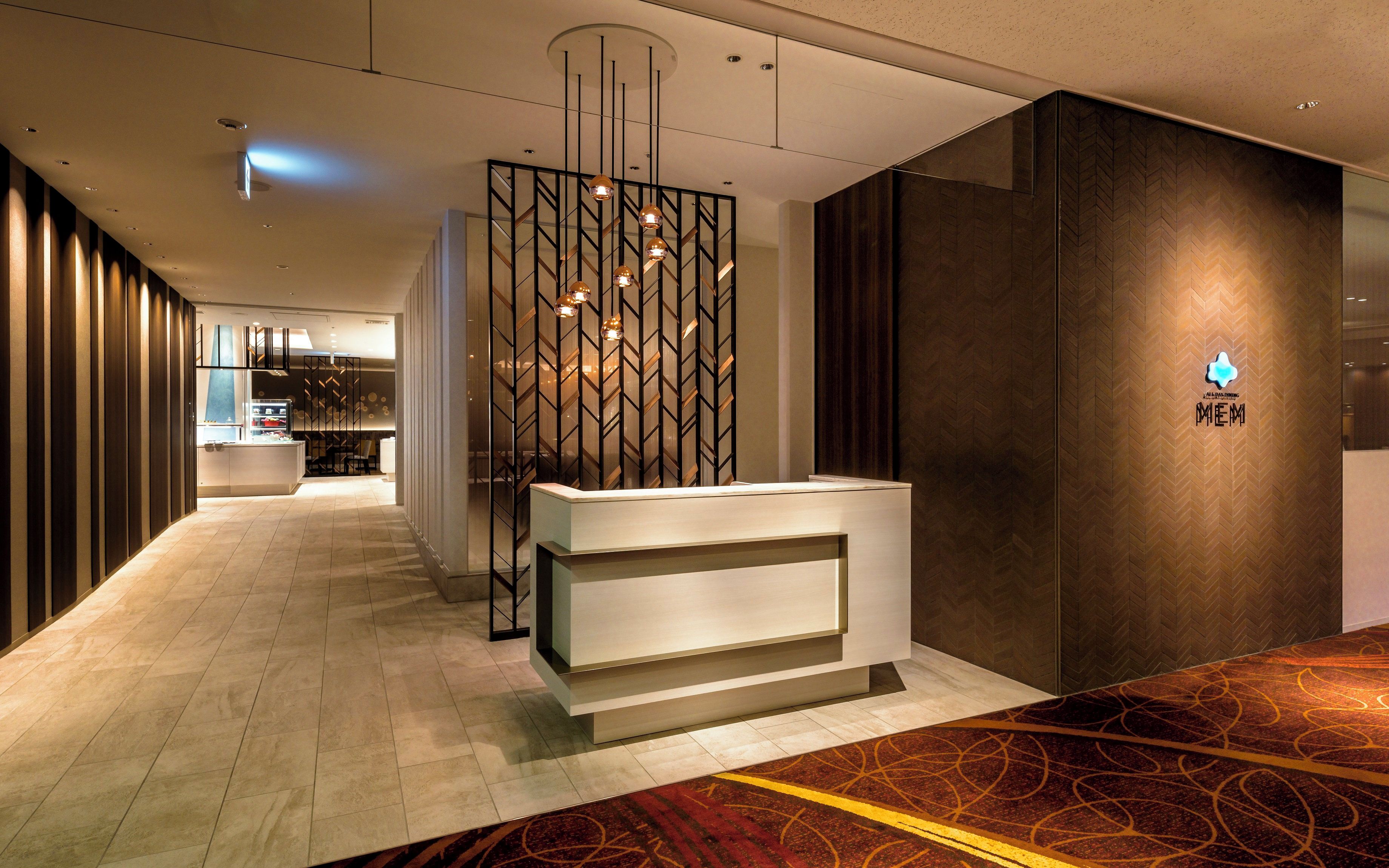 A modern hotel reception area with a reception desk, a decorative wall with a geometric pattern, and a herringbone-patterned wall.
