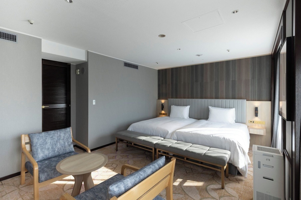A hotel room with a large bed, a seating area with a table, and a window.