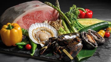 A variety of seafood including a whole fish, lobster, and oysters, along with vegetables like asparagus, bell peppers, and corn.