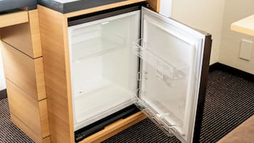 A compact refrigerator with a transparent door, built into a wooden cabinet with a black countertop above.