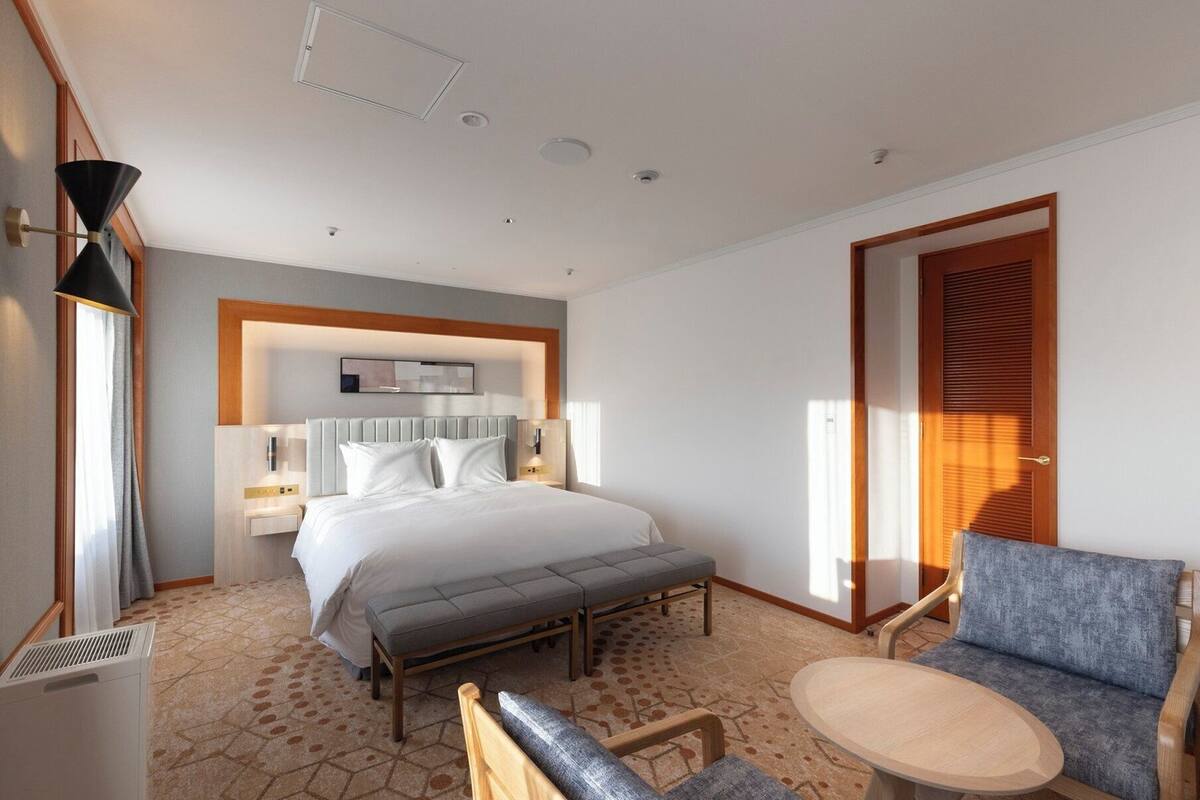 A hotel room with a bed, bedside table, chair, and a small table.