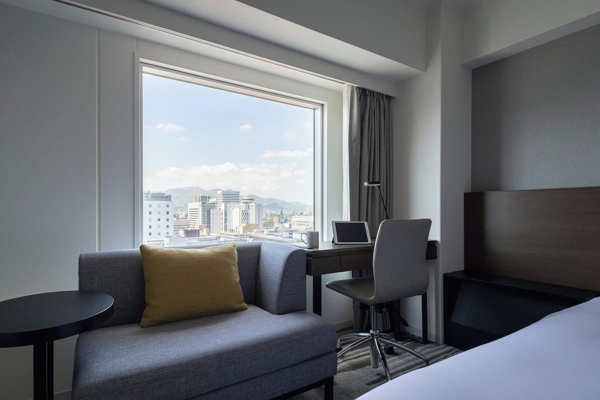 A hotel room with a sofa, a desk with a laptop, a chair, and a bed.
