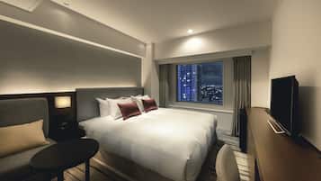 A hotel room with a large bed, a desk, a chair, a TV, and a window with a city view.