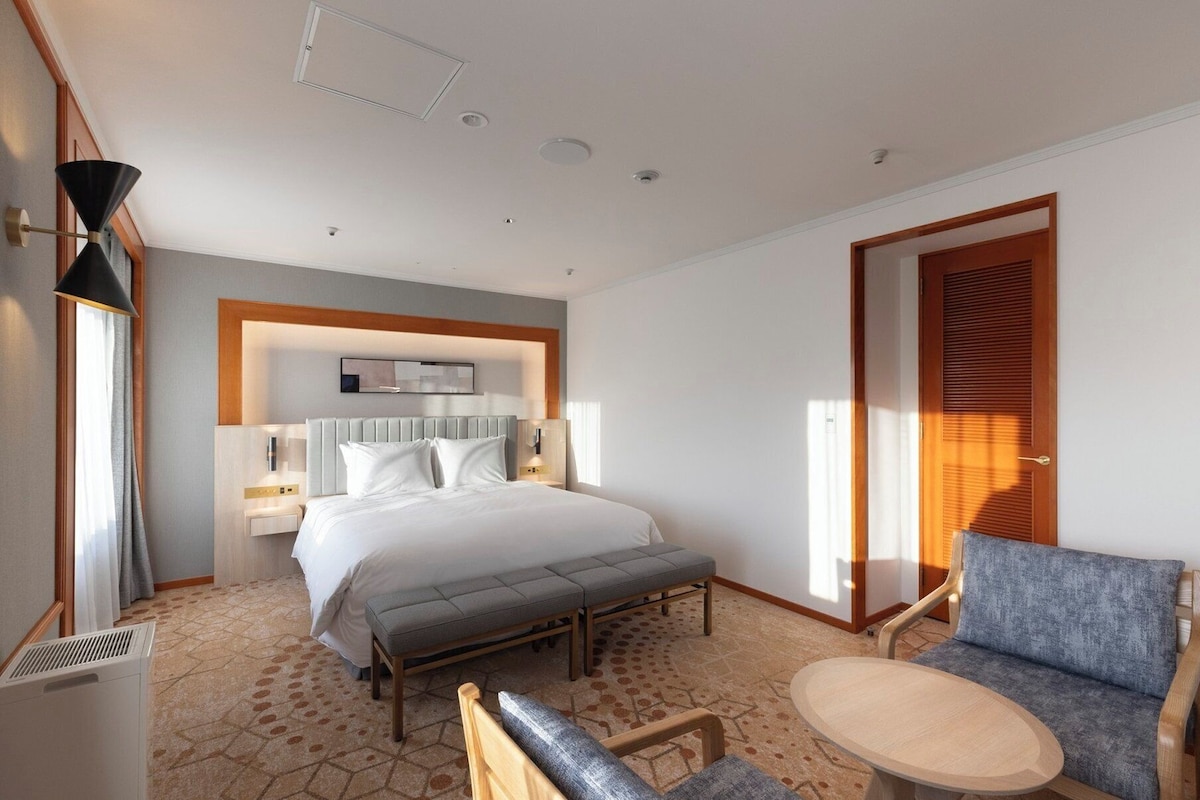 A hotel room with a bed, bedside table, chair, and a small table.