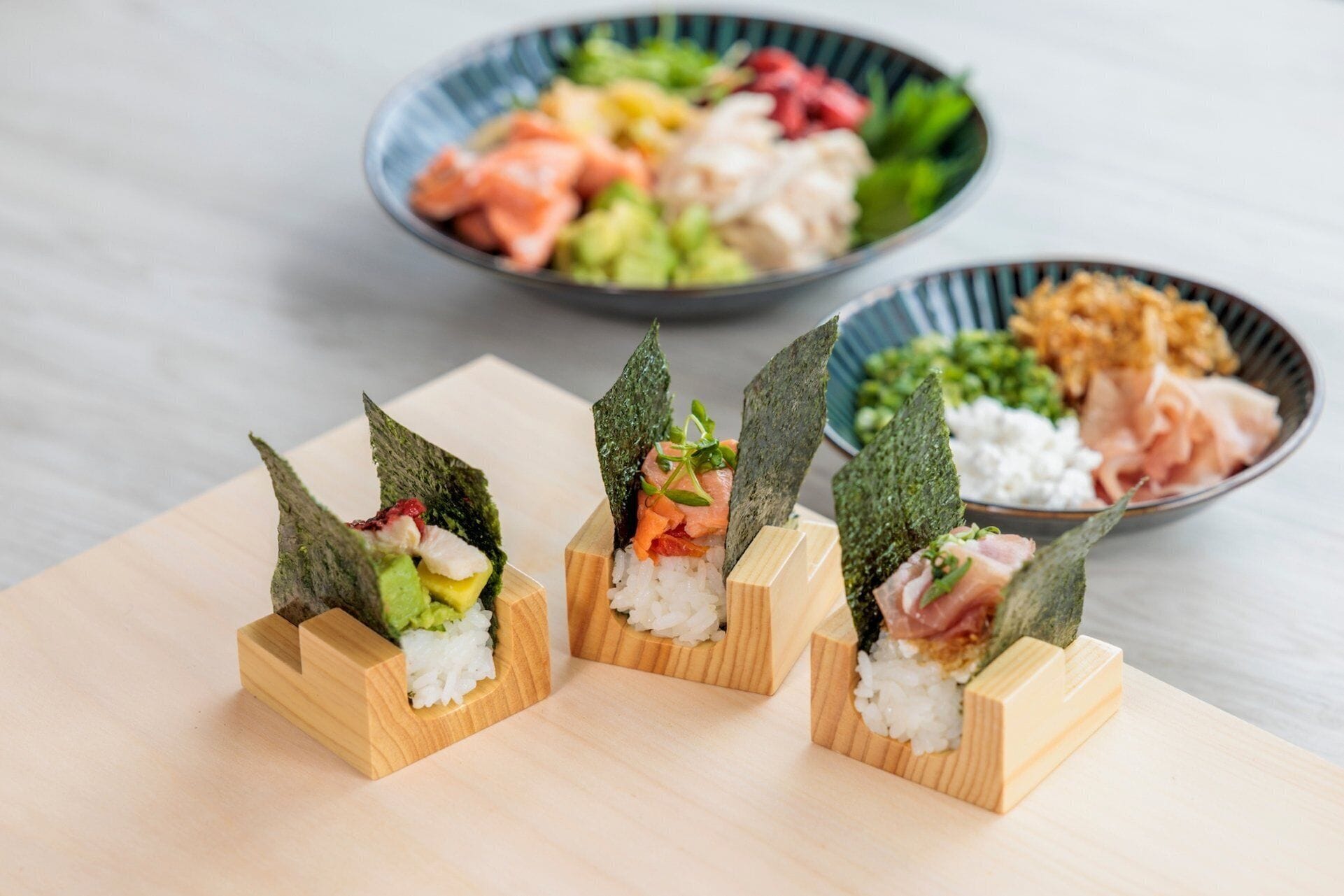 Three sushi pieces on wooden stands with seaweed on top.