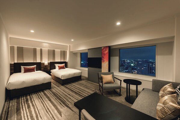 A modern hotel room with two beds, a sofa, a chair, and a TV.