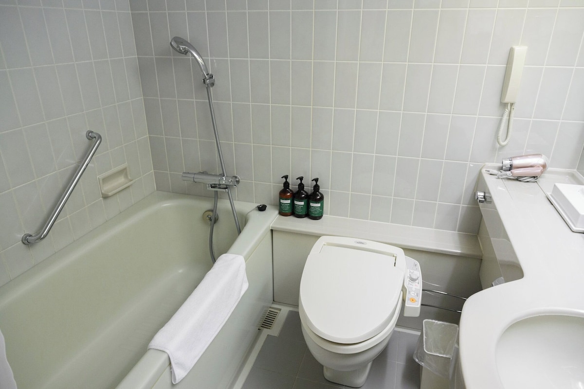 A bathroom with a bathtub, a toilet, and a shower. There are bottles of toiletries on the counter.