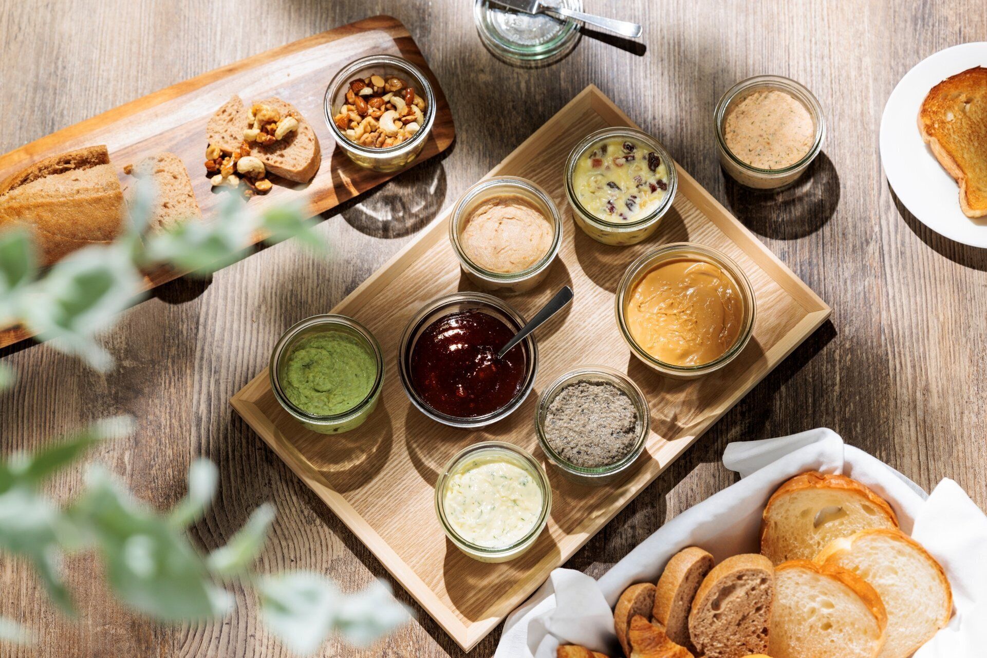 A wooden board with various food items and condiments, including bread, nuts, and jars of spreads.