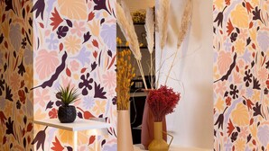 A room with a floral wallpaper design, a shelf with a potted plant, and two vases with dried plants. - Hotel Elysees 8 (Paris)