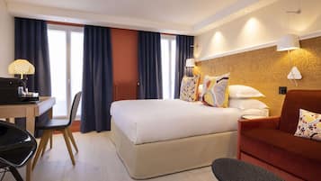 Ein Hotelzimmer mit Bett, Schreibtisch, Stuhl, Sofa und einem Fenster mit Vorhängen.