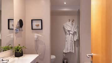 Un baño moderno con lavamanos, espejo y fotografías enmarcadas. Hay un inodoro y una zona de ducha con una bata colgada.