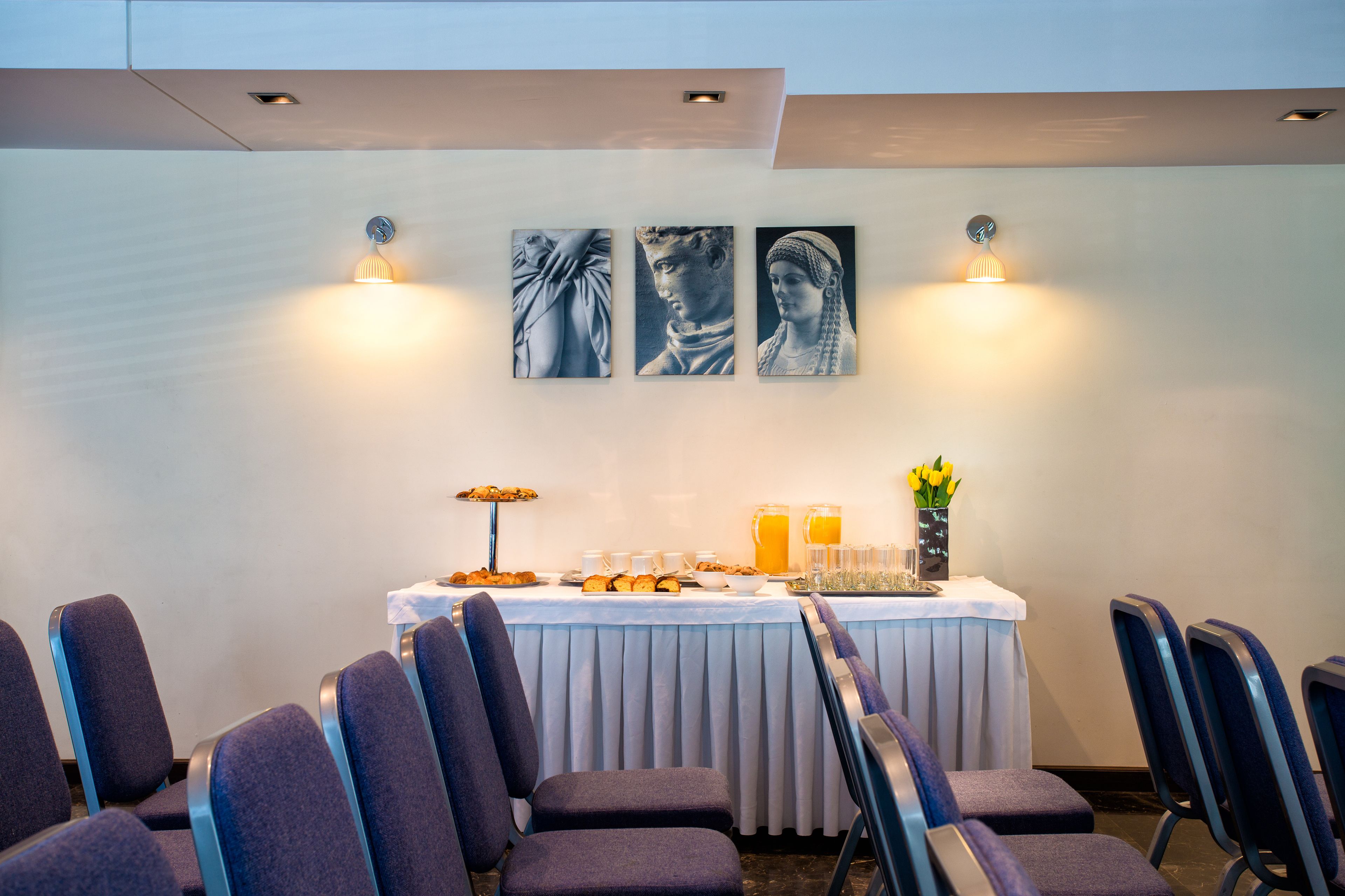 Une salle de conférence avec une table préparée pour une réunion, des chaises disposées autour, et des œuvres d’art accrochées aux murs.
