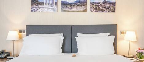 Quarto de hotel com uma cama grande, duas luminárias de cabeceira e três quadros na parede.