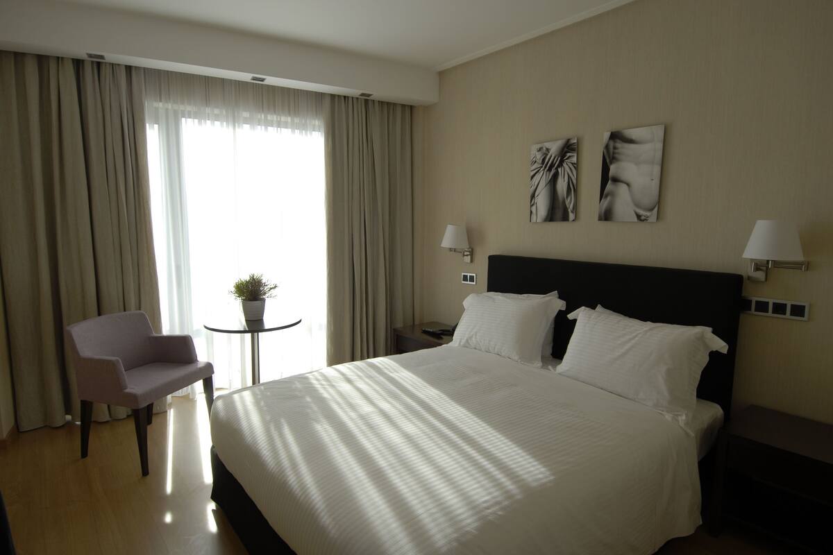 Camera d'albergo con un letto grande, una poltrona, un tavolino con una pianta e due lampade a parete.