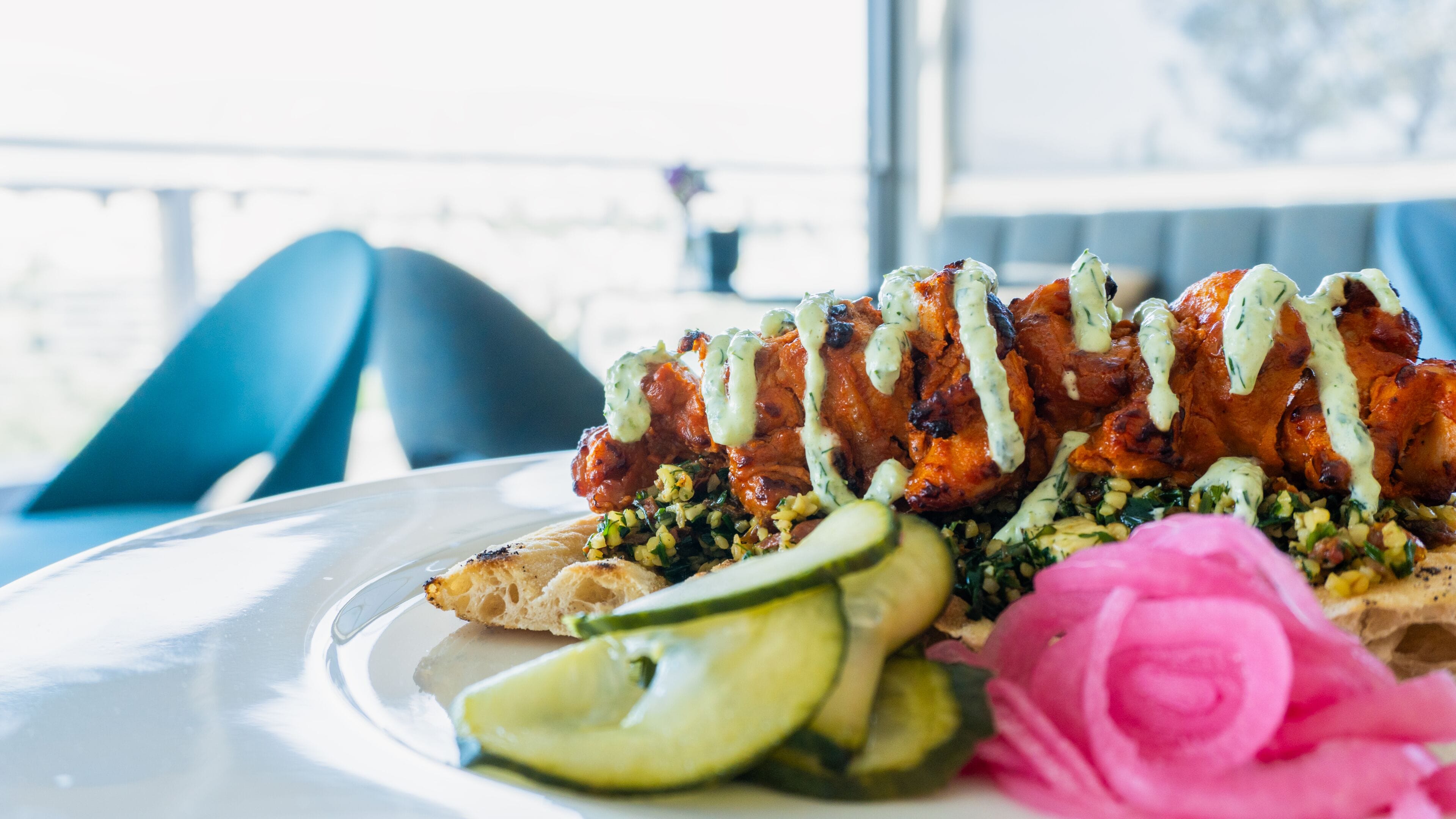 A plate of food with a pink flower garnish, a slice of cucumber, and a piece of bread.