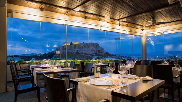 An outdoor dining area with tables set for two, overlooking a historic site. - Athens Gate Hotel (Athens)