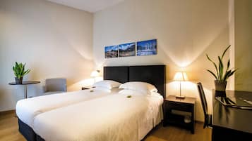 A hotel room with two beds, a desk, a chair, a lamp, and a potted plant.