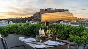 A rooftop dining table set with plates, cutlery, and wine glasses, overlooking a cityscape with a prominent ancient structure in the background. - Athens Gate Hotel (Athens)