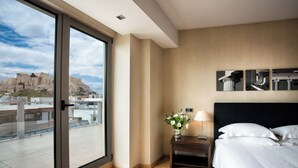 A hotel room with a large sliding glass door leading to a terrace, a bed with white linens, a nightstand with a lamp, and a wall-mounted picture of ancient architecture. - Athens Gate Hotel (Athens)
