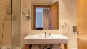 Un baño moderno con ducha de vidrio, un lavamanos blanco con un espejo encima y un mueble de tocador de madera con toallas.