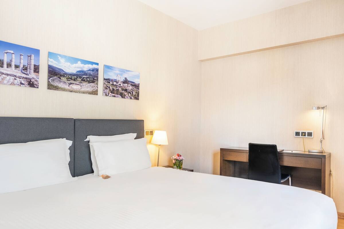 Una camera d'albergo con un letto grande, una scrivania e una sedia. Tre quadri sono appesi alla parete.