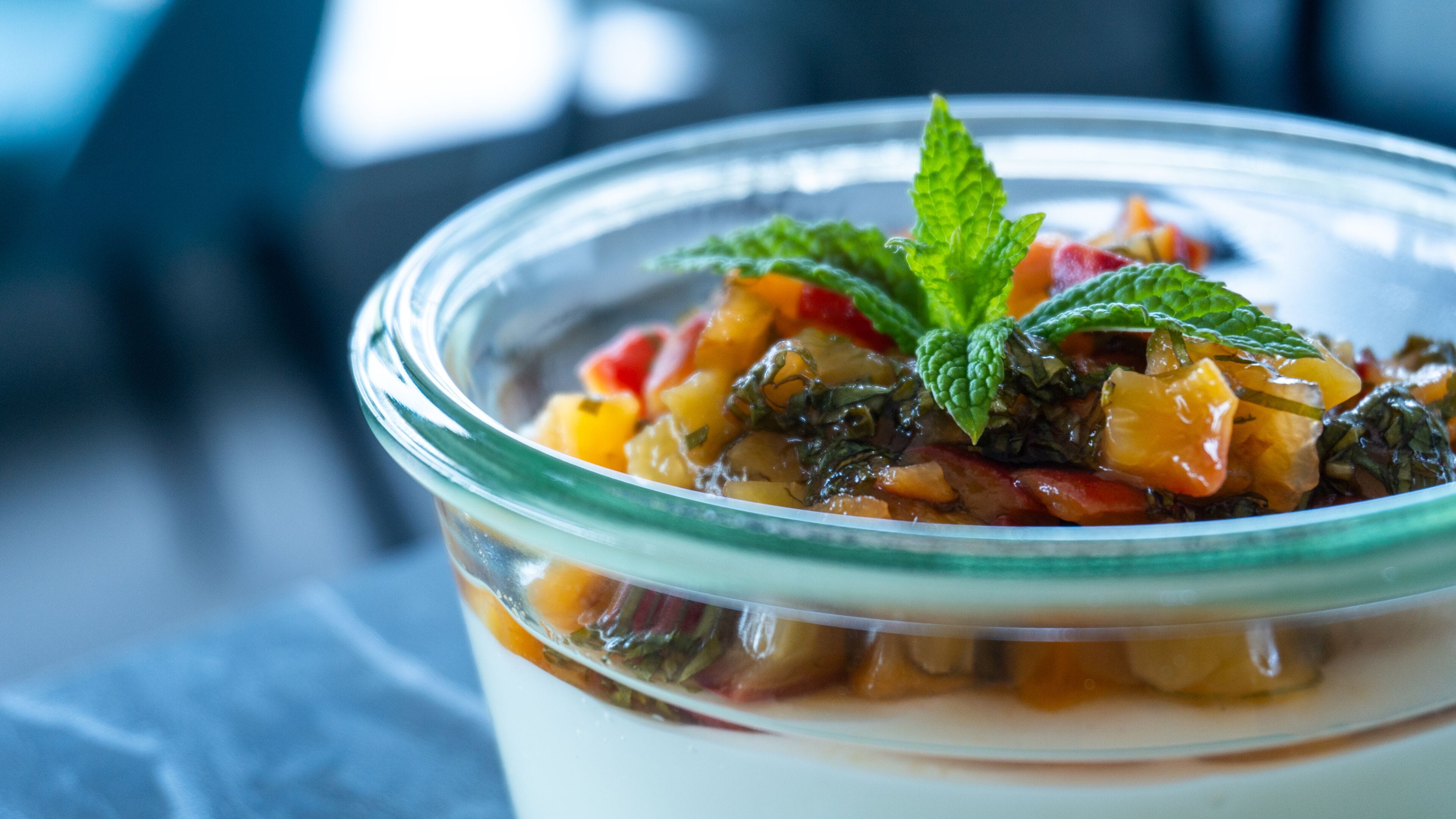A clear glass bowl with a layered dessert, garnished with mint leaves.