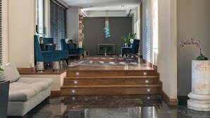 A modern living room with a fireplace, blue armchairs, a grey sofa, and a staircase leading to another level. - Athens Gate Hotel (Athens)