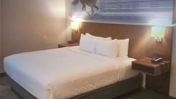 A hotel room with a large bed, two bedside tables, a mounted artwork, and two wall-mounted lamps.