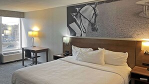 A hotel room with a large bed, a desk, a chair, and a wall-mounted TV.