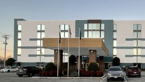 A modern building with a flat roof, large windows, and a parking lot with several cars.