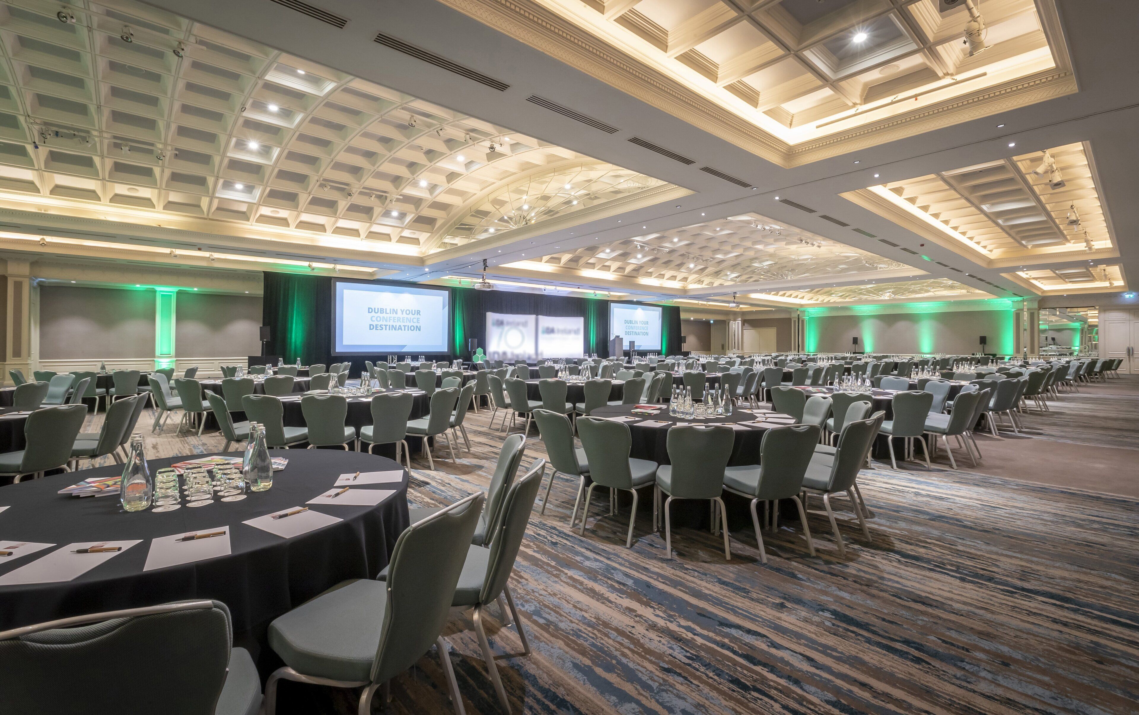 A large conference room with multiple tables and chairs, a projection screen, and a high ceiling with skylights.