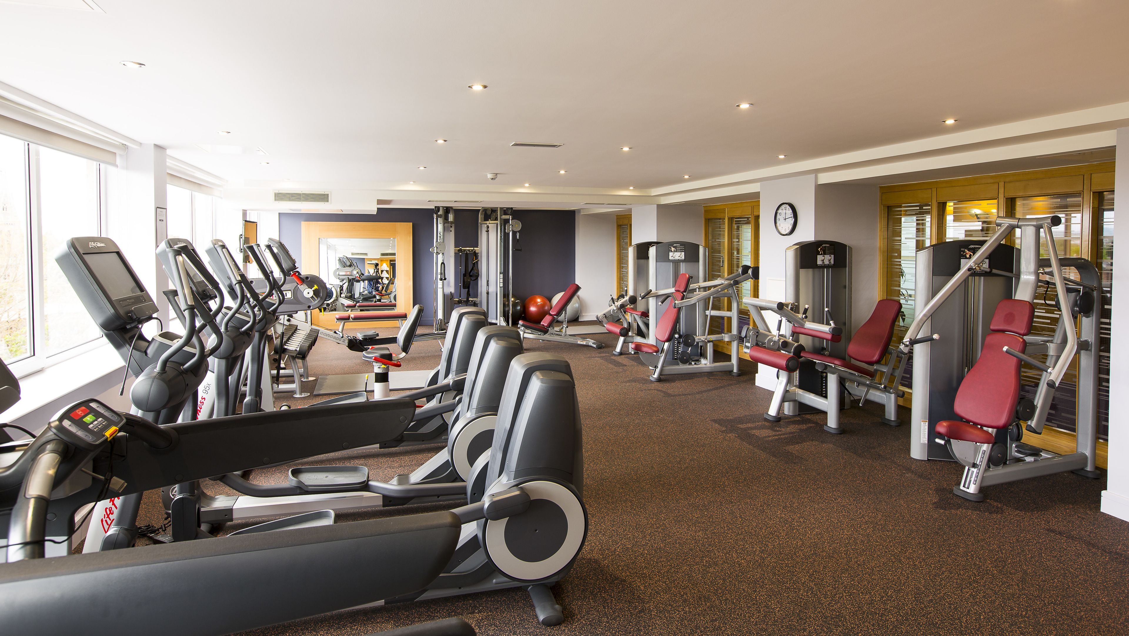 A gym with various exercise machines, a mirrored wall, and a clock on the wall.